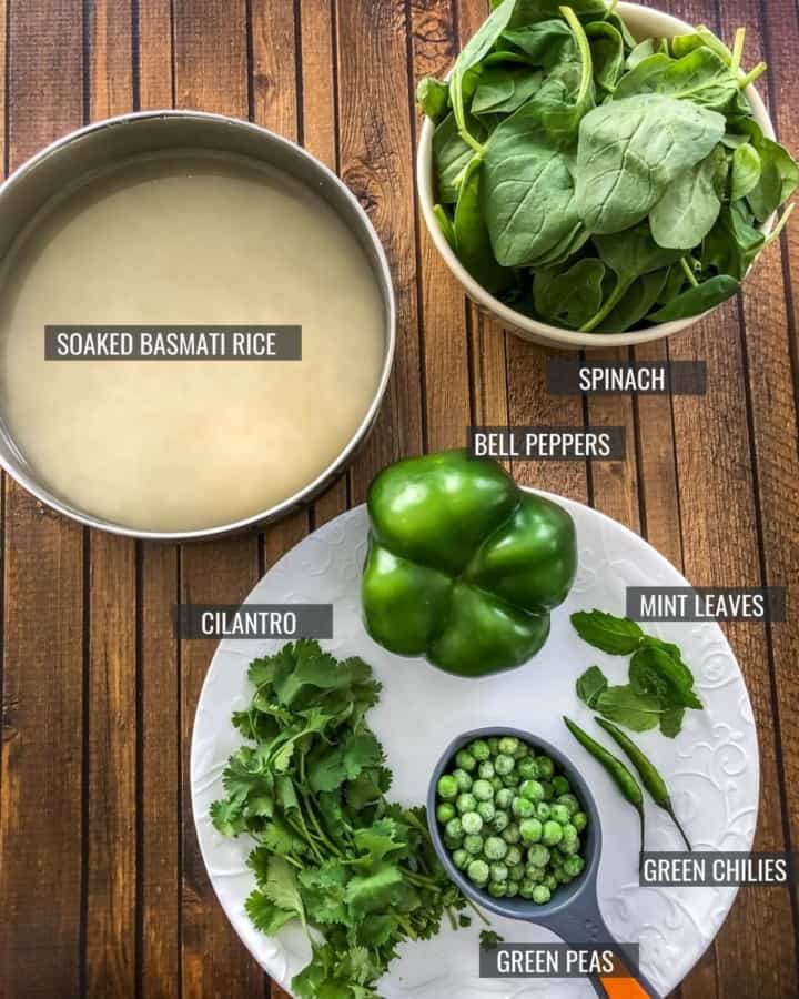 A bowl of rice soaking in water at the top left next to a bowl of fresh baby spinach in the top right, and a plate at the bottom middle with a bell pepper, cilantro, peas, and mint leaves on a wooden counter.