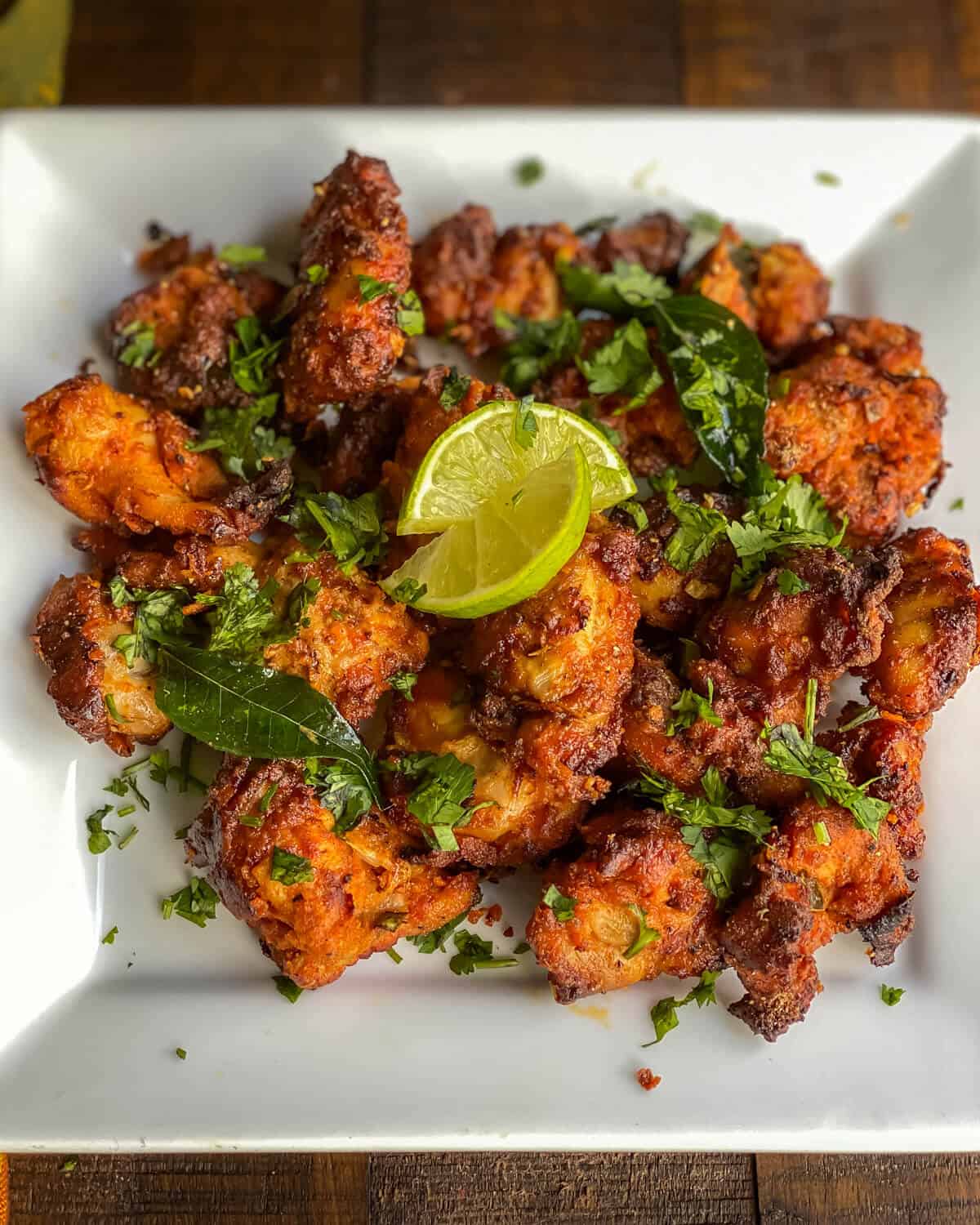A white plate topped with chicken 65 pieces sprinkled with cilantro and lemon wedges.