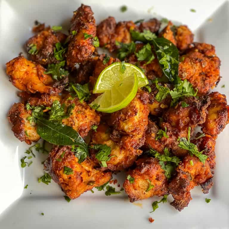 A white plate with an array of crispy chicken 65 topped with cilantro and lemon.