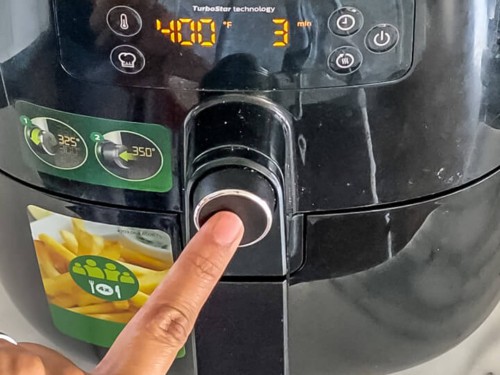 A hand pushing the preheat button on the air fryer at 400°F.