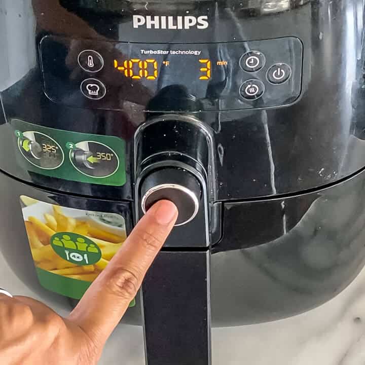 A hand pushing the preheat button on the air fryer at 400°F.