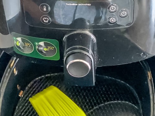 A brush coating the air fryer basket with oil.