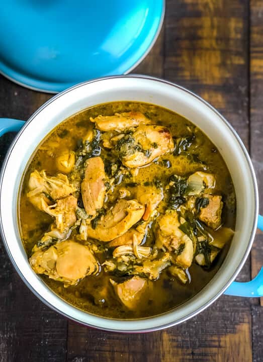 A blue bowl with handles on the side filled with methi chicken on a wooden counter.