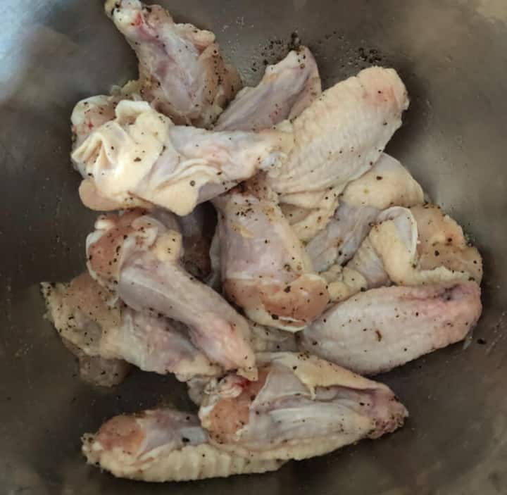 Chicken wings coated in oil, salt, and pepper in a bowl.