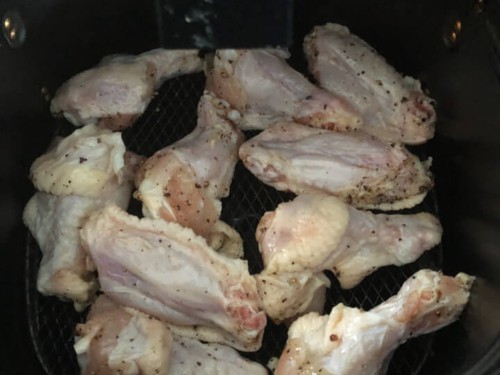 Chicken wings in a single layer in the frying basket of an air fryer.