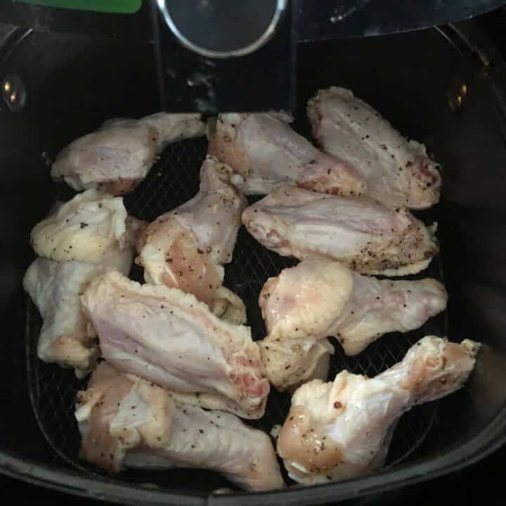 Chicken wings in a single layer in the frying basket of an air fryer.