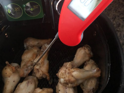 An instant read thermometer checking the internal temperature of the chicken in the air fryer.
