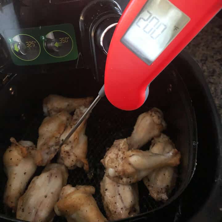 An instant read thermometer checking the internal temperature of the chicken in the air fryer.