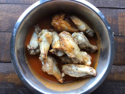 Chicken wings in a bowl with buffalo sauce.