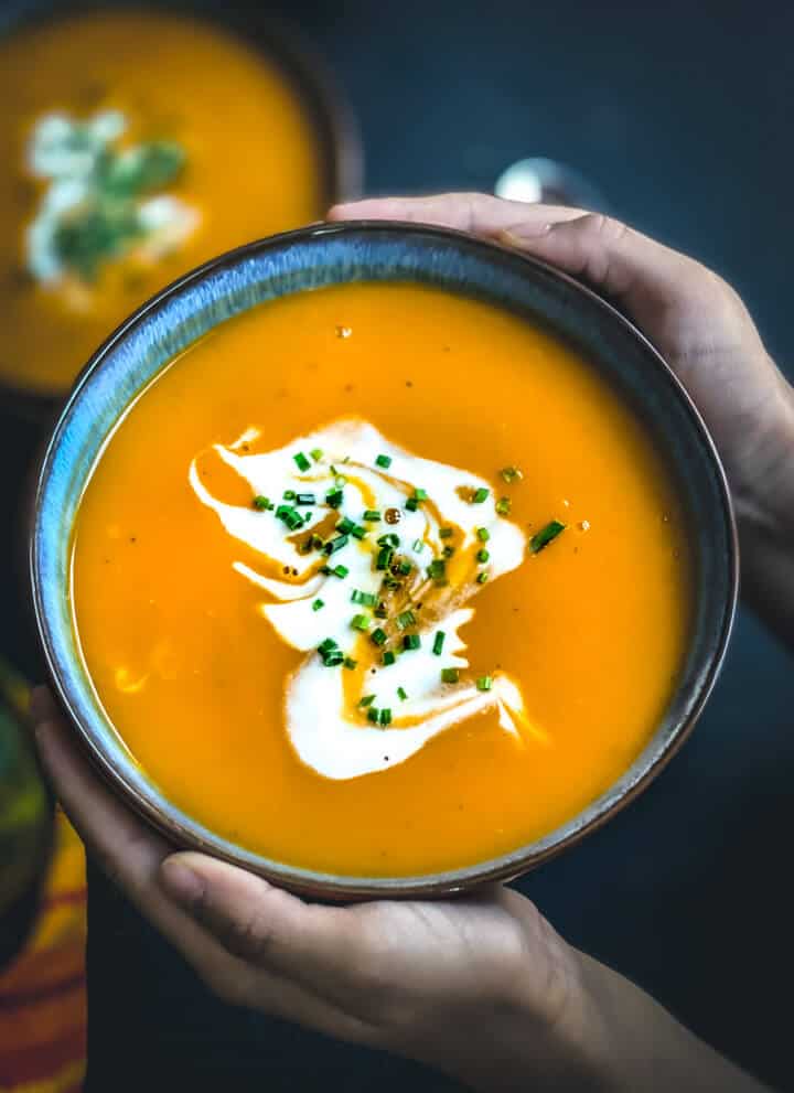 Two hands holding a blue bowl filled with instant pot butternut squash soup topped with coconut milk and chive.