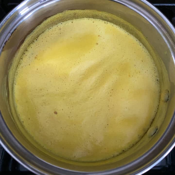 Golden milk boiling in a saucepan on a stove.