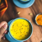 A hand holding a blue mug filled with golden turmeric milk with the words Golden Turmeric milk at the top of the image.