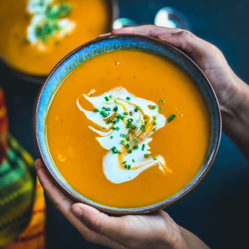 A square photo of Instant pot butternut squash soup in a blue bowl being held by two hands.