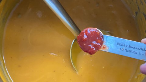 A teaspoon with chili paste going into the soup.