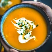 Two hands holding a blue bowl filled with instant pot butternut squash soup topped with coconut milk and chive with the words vegan and instant pot butternut squash soup at the top.