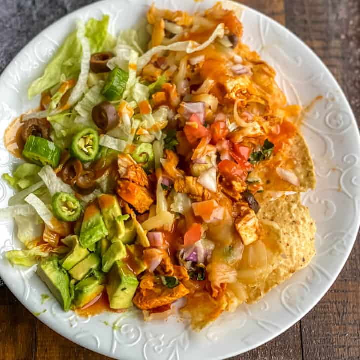 A white plate with buffalo chicken nachos topped with shredded lettuce.