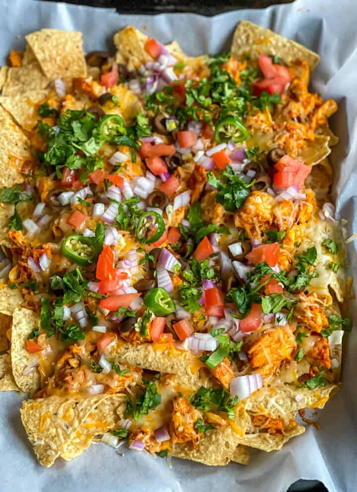 A sheet pan covered in parchment paper and topped with buffalo chicken nachos.