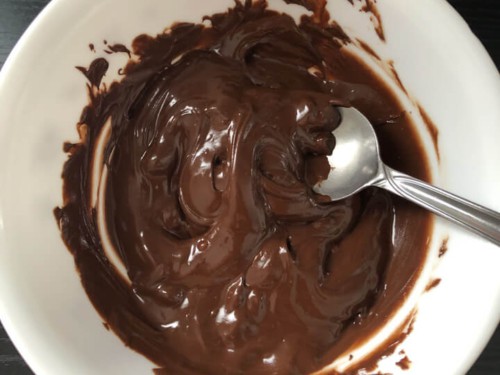 A white bowl with melted chocolate being stirred by a spoon.