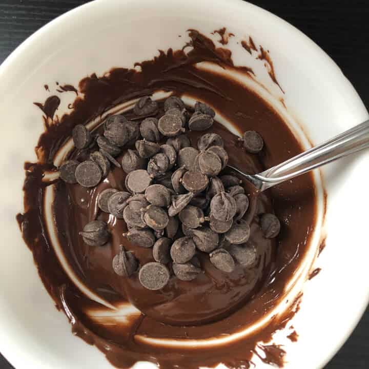 Chocolate chips on top of melted chocolate with a silver spoon.