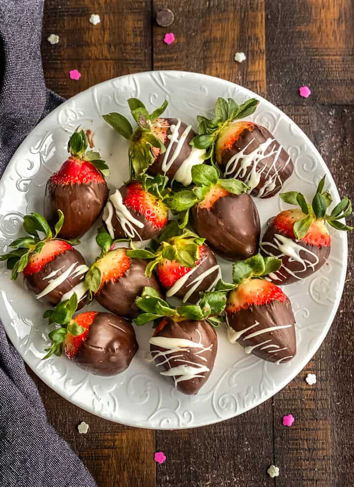 A white plate on a wooden counter with chocolate covered strawberries on the plate. 