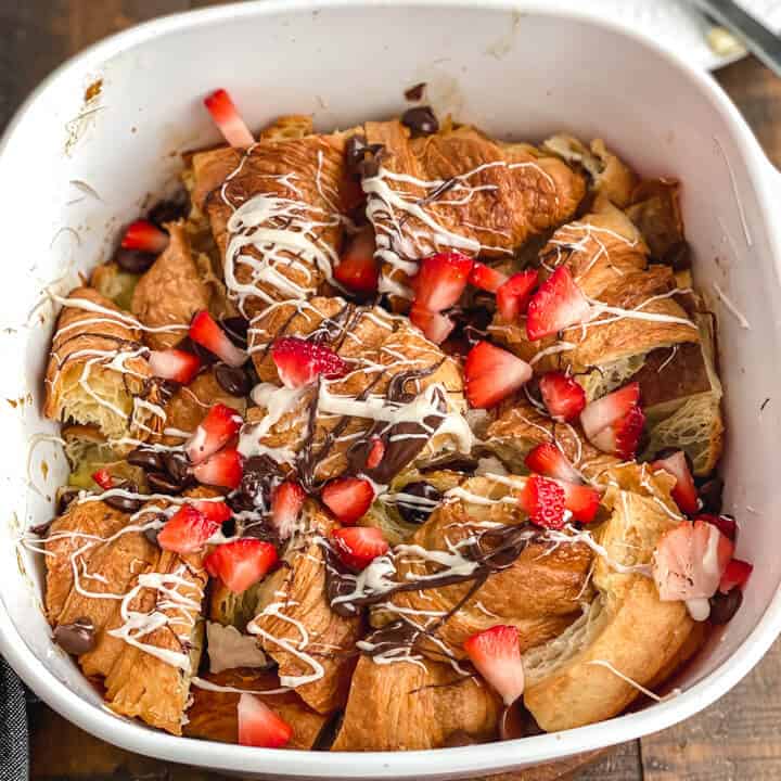 A white baking dish with chocolate croissant bread pudding topped with melted chocolate and fresh fruit.