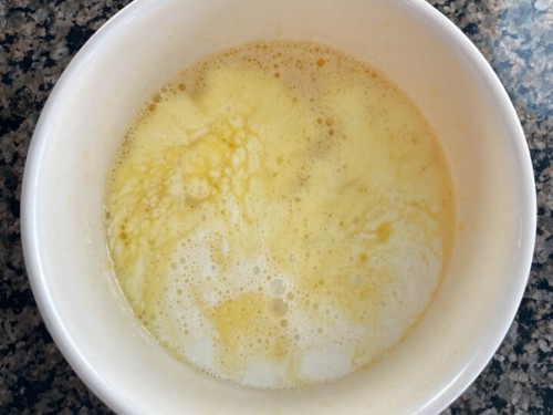 A white bowl with frothy eggs topped with milk, sugar, and vanilla mixed in.
