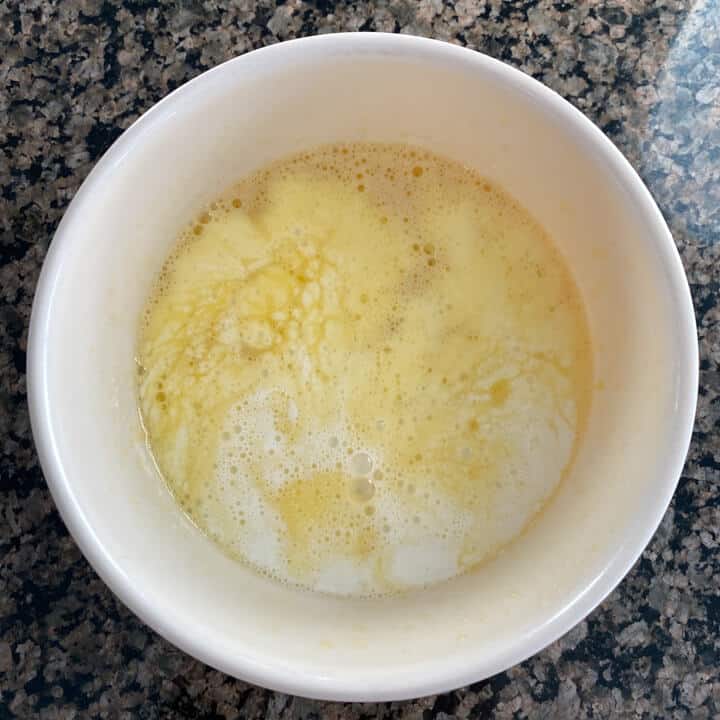 A white bowl with frothy eggs topped with milk, sugar, and vanilla mixed in.