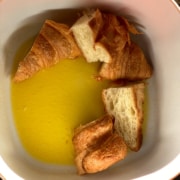 A white baking dish with melted butter and pieces of chopped croissant.