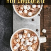 Two white mugs of hot chocolate topped with marshmallows on a marble cutting board with the words Homemade Hot Chocolate at the top.