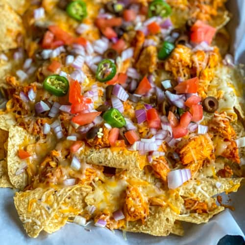 A plate lined with parchment paper and topped with loaded buffalo chicken nachos.