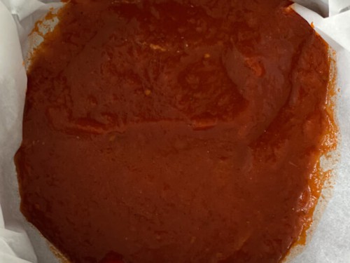 A springform pan lined with parchment paper with a scoop of marinara sauce.