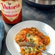 A white plate with a serving of vegetarian lasagna with a fork and a jar of victoria marinara sauce in the back with the words Instant Pot Lasagna in the top right.