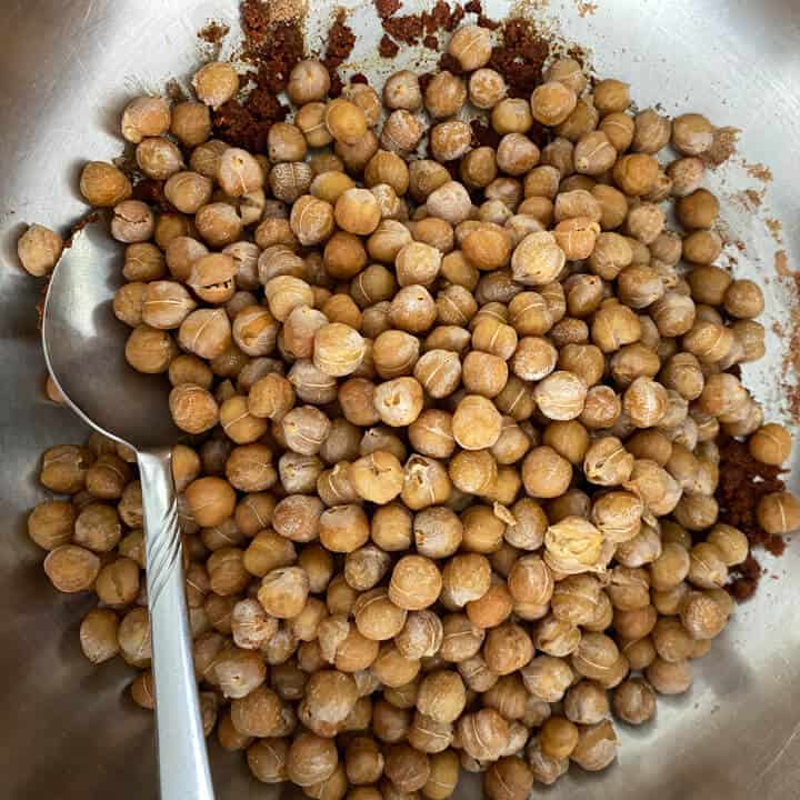 Chickpeas in a bowl with a spoon being coated with the oil and spice blend.