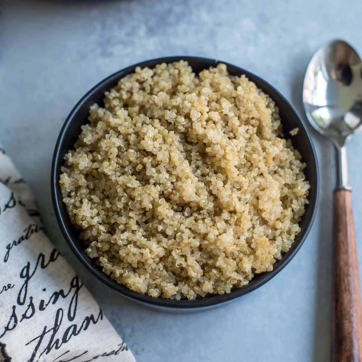 A black bowl with fluffy quinoa and a silver spoon with a wooden handle to the right.