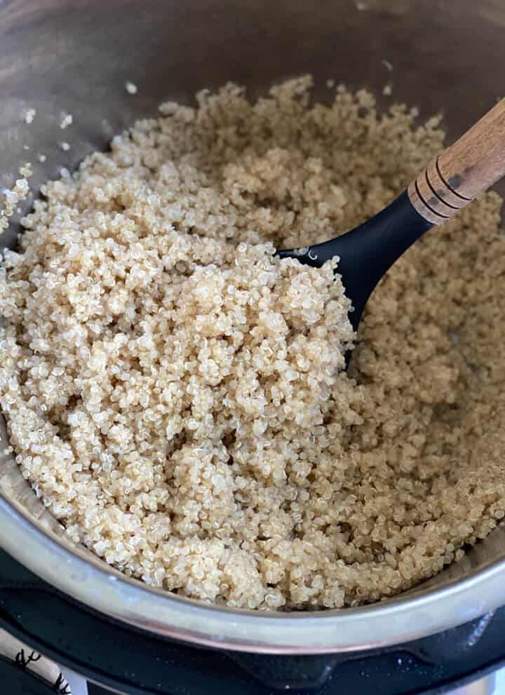 The instant pot with fluffy cooked quinoa and a large spoon to the top left.