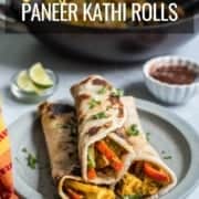 A light blue plate with three paneer kathi rolls stacked in a pyramid with a small white bowl of tamarind chutney in the back right and the words Easy Panner Kathi Rolls at the top.