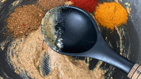 Spices added to the wok with the paste and the spoon.