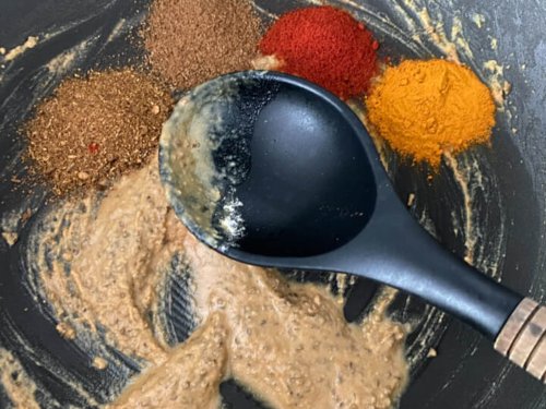 Spices added to the wok with the paste and the spoon.
