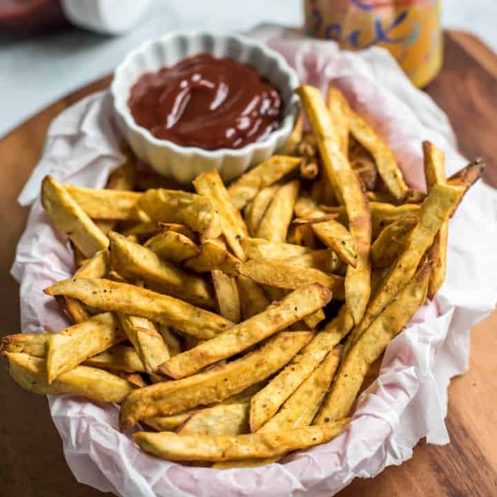 A basket covered in parchment paper with sweet potato fries and a small white bowl of ketchup.
