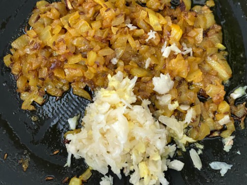 Garlic and ginger being added to the skillet with the onion and spices.