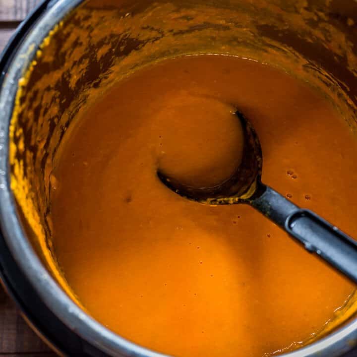 A black spoon in an instant pot with tomato basil soup.