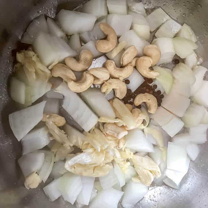 The base of the instant pot with onion, garlic, cashews, and peppercorns.