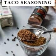 Spoon of taco seasoning on top of a glass cup with seasoning bottles on the side