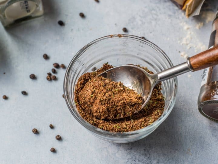 Spoon of taco seasoning in a glass bowl with black peppercorns on the side