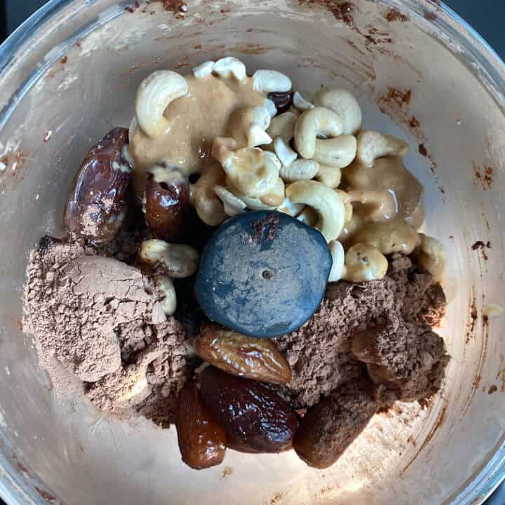 A food processor with all of the ingredients for chocolate energy date balls.
