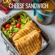 grilled cheese sandwich in a lunch box with salad and tomato soup
