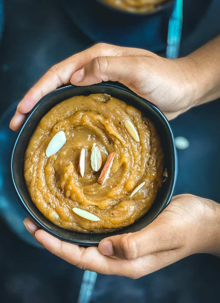 the author's hands holding a bowl of this homemade moong dal halwa recipe topped with chopped almonds