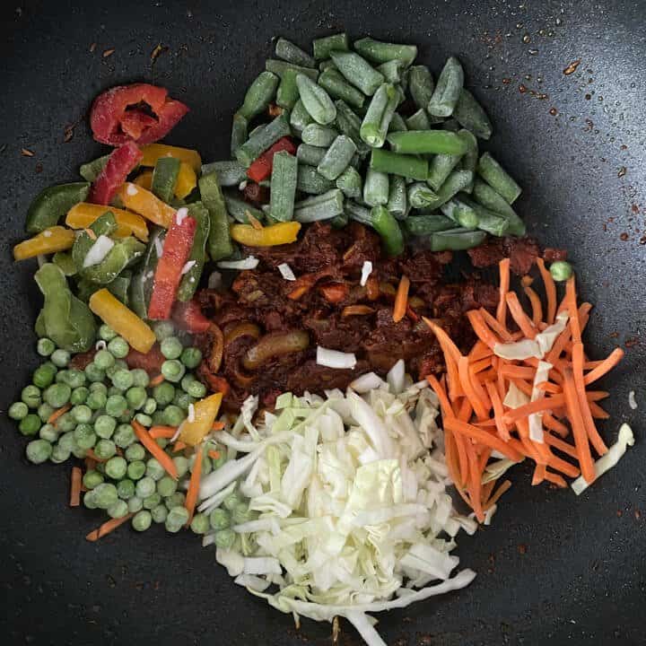 Beans, bell pepper, cabbage, carrots, peas added to onion-tomato masala