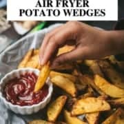 A hand dipping a potato wedge in ketchup