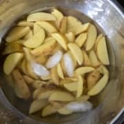Potato wedges soaked in iced water in a steel bowl